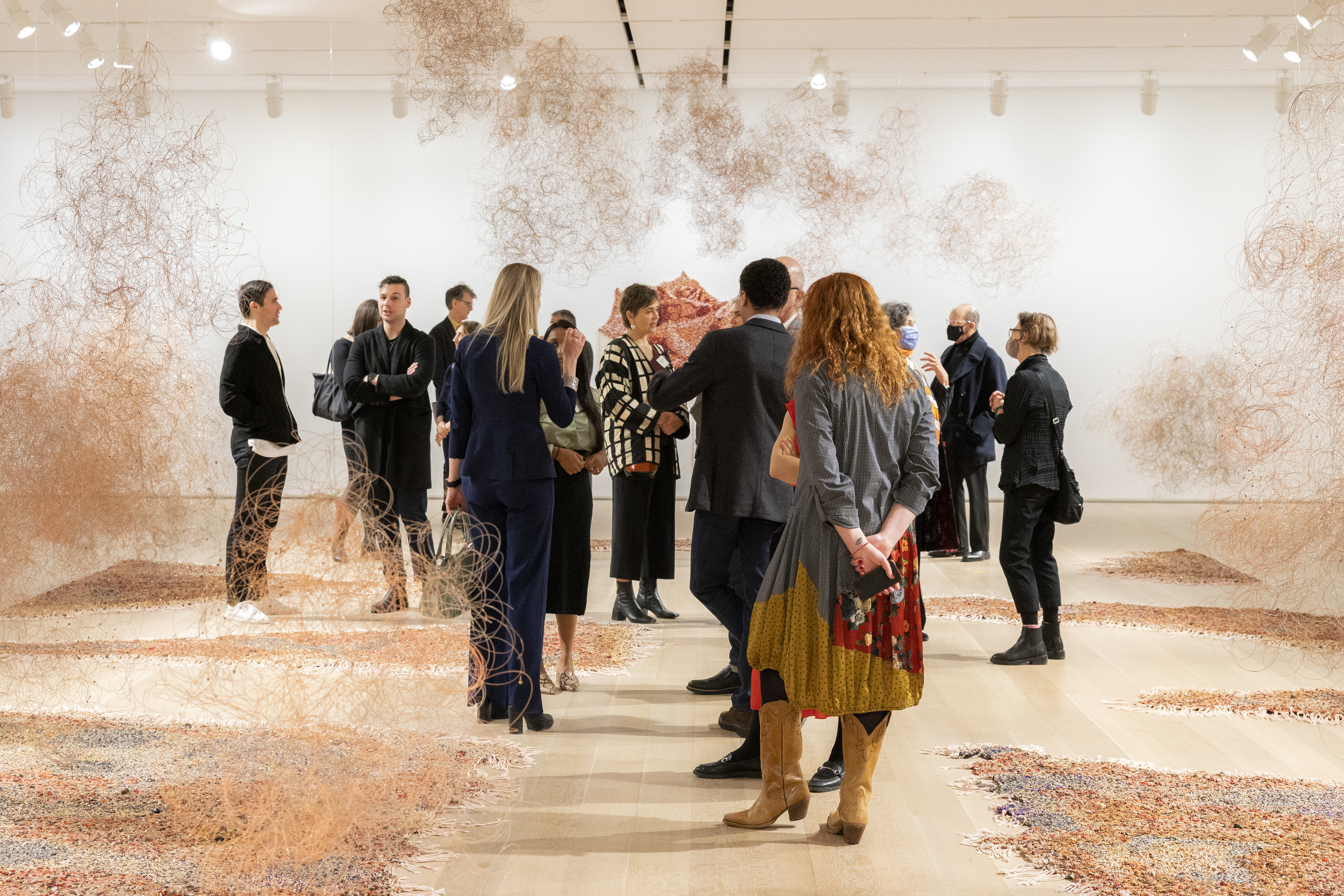 People view artwork made of beads installed on a wooden floor and hung from the ceiling.